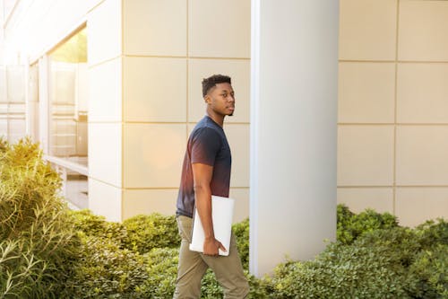 Man Walking Beside Green Leafed Plants Near White Concrete Pillar