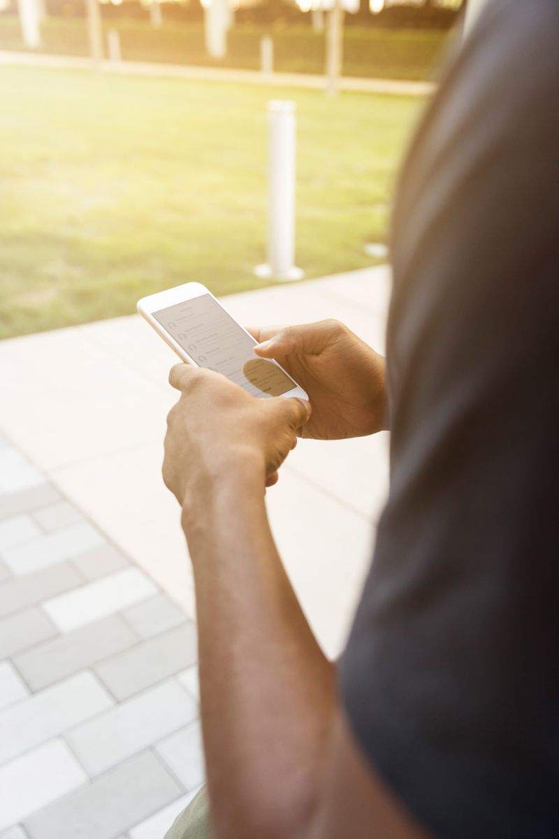 A close-up view of a person texting on a smartphone in a sunlit outdoor setting