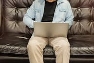 穿着休闲装的男人坐在室内的真皮沙发上，用笔记本电脑工作，传达出放松和舒适的感觉