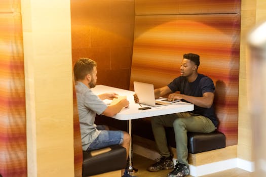 Two men discussing work at a laptop in a modern indoor workspace setting.