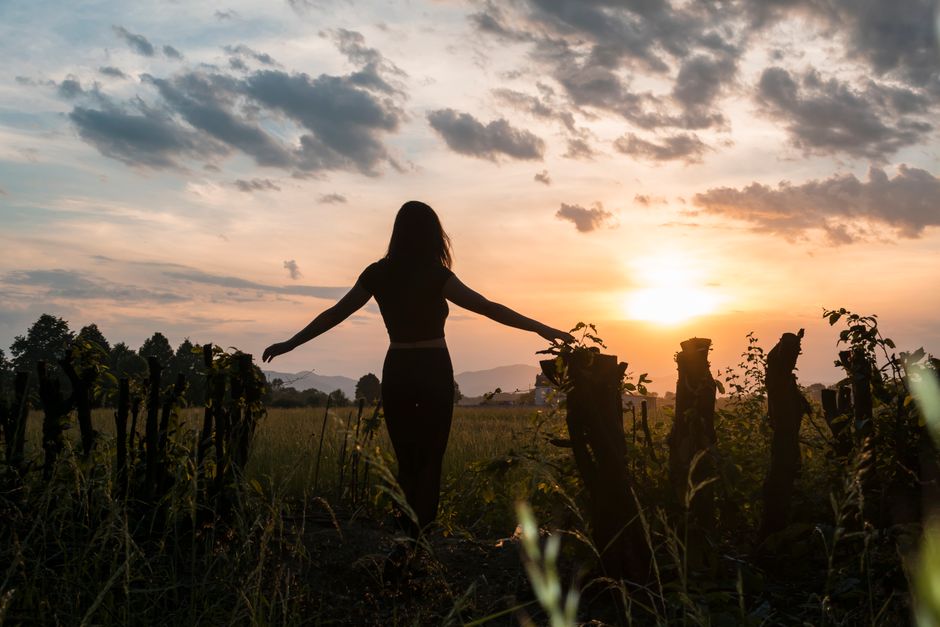 A woman stands in a field at sunset, arms outstretched, capturing a serene moment of release and freedom