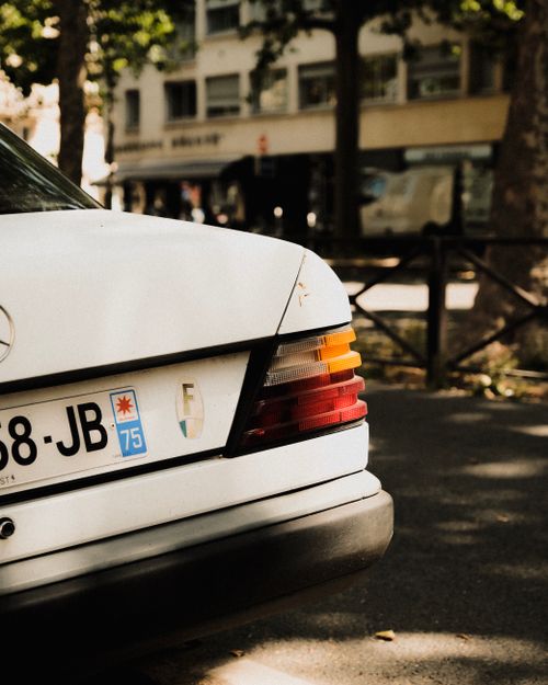 Free Close-up of a classic Mercedes-Benz tail light with license plate, captured under a tree-lined street. Stock Photo