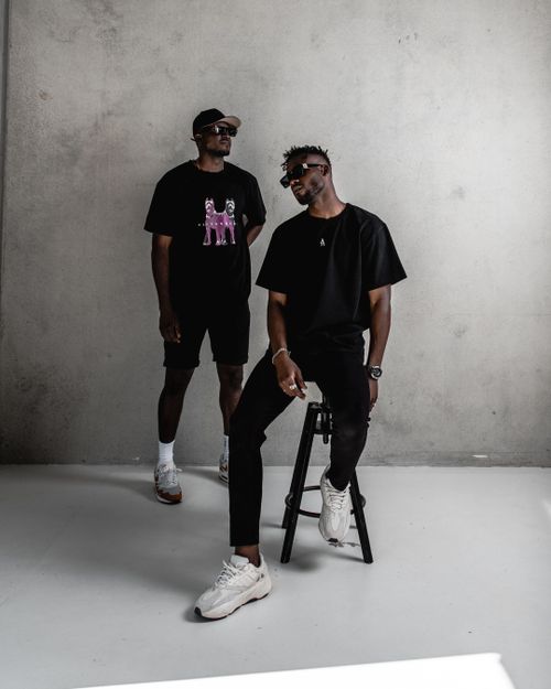 Free Two stylish men in black T-shirts and sneakers pose against a gray concrete wall. Stock Photo