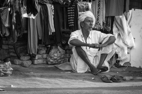 Free Elderly man sitting in a traditional market scene in grayscale. Stock Photo
