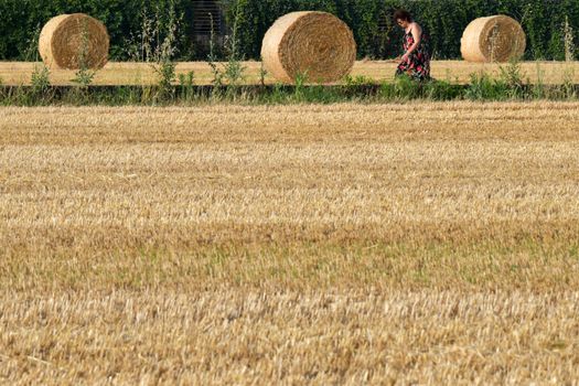 A serene countryside scene featuring a woman walking amid hay bales in Rizza, Veneto, Italy.