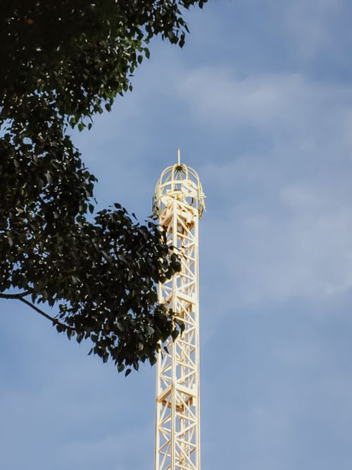 Free A sleek modern tower rises against a clear blue sky framed by green foliage. Stock Photo