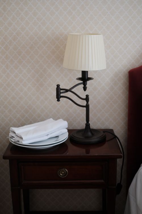 Free A neatly arranged bedside table featuring a classic lamp and folded linens for a cozy ambiance. Stock Photo