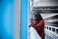 一名年轻女子靠在桥栏杆上，若有所思地凝视着城市景观