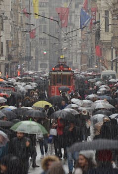 A vibrant city street scene with a crowd holding umbrellas in the rain.