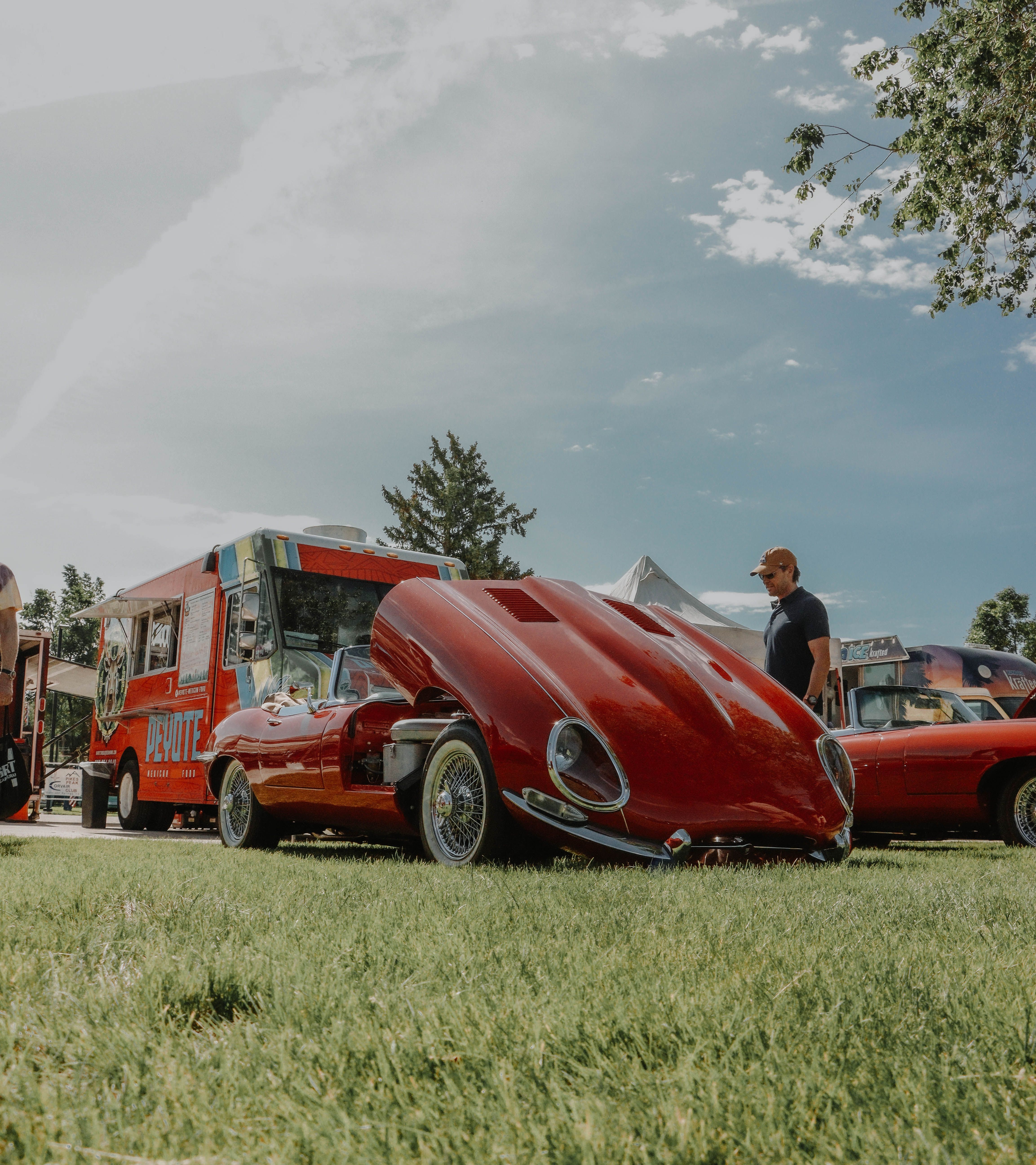 Red convertible car on display at outdoor event with food trucks and people.