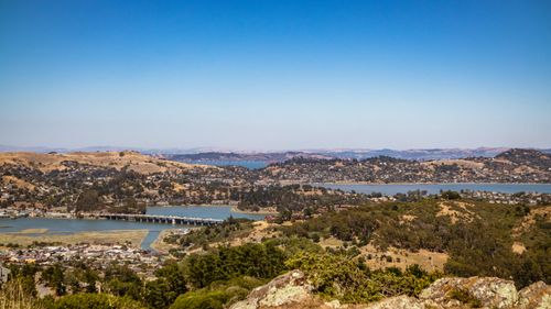 Free A stunning aerial view of a bridge spanning a river, surrounded by rolling hills and clear skies. Stock Photo