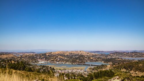 Free A breathtaking aerial view capturing rolling hills and a lake under a clear blue sky. Stock Photo