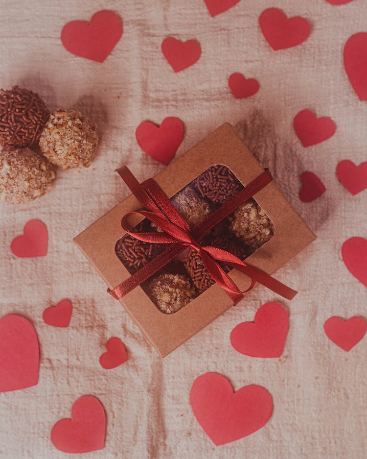 Box With Sweet Treats Among Red Heart Shapes