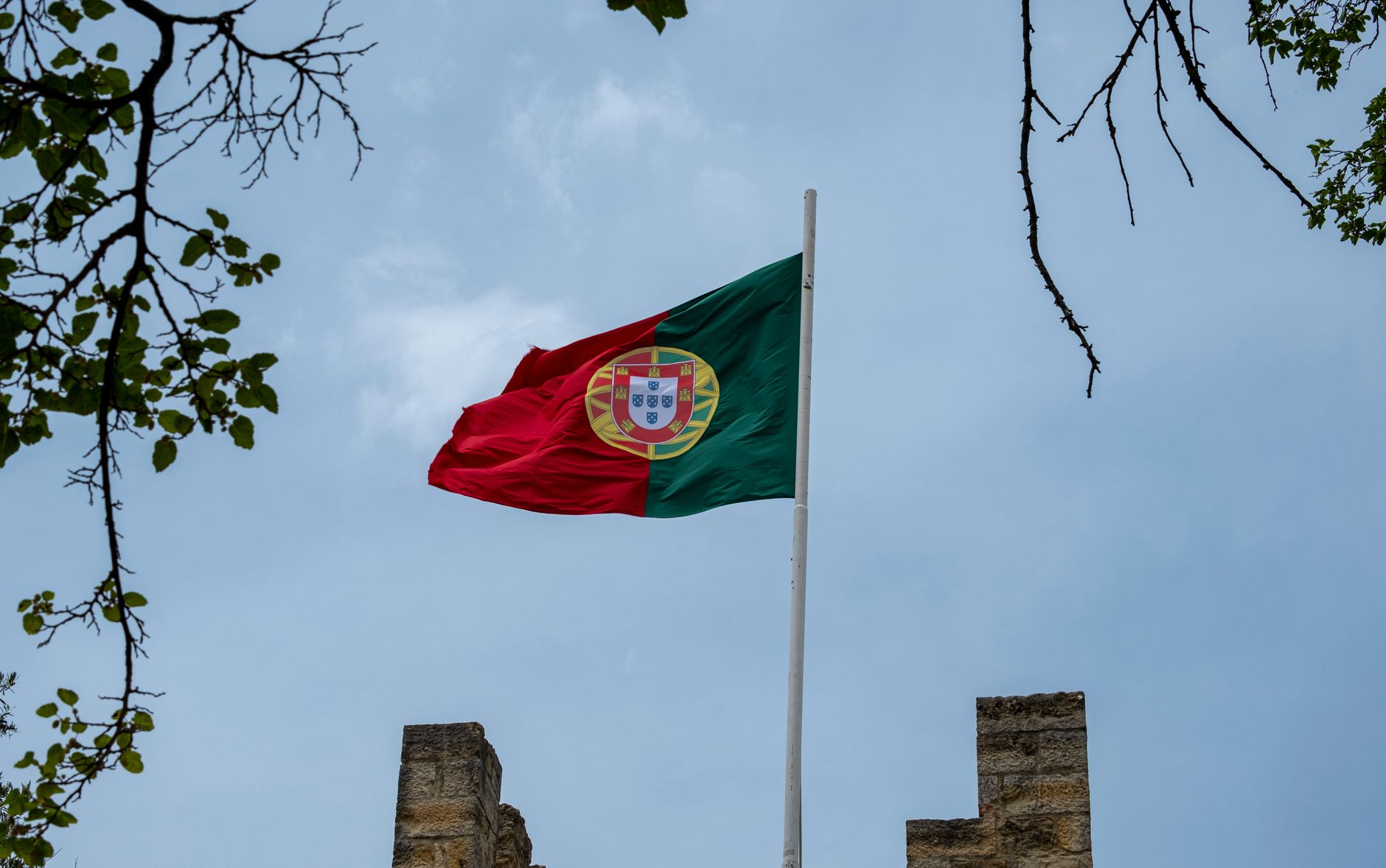 The Portuguese flag on a pole with a serene blue sky background.