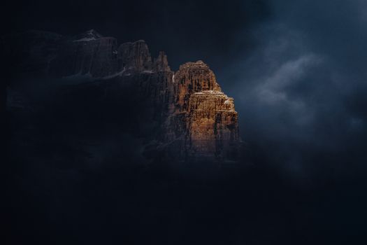 Stunning mountain peak highlighted through dramatic clouds, showcasing nature's beauty at twilight.