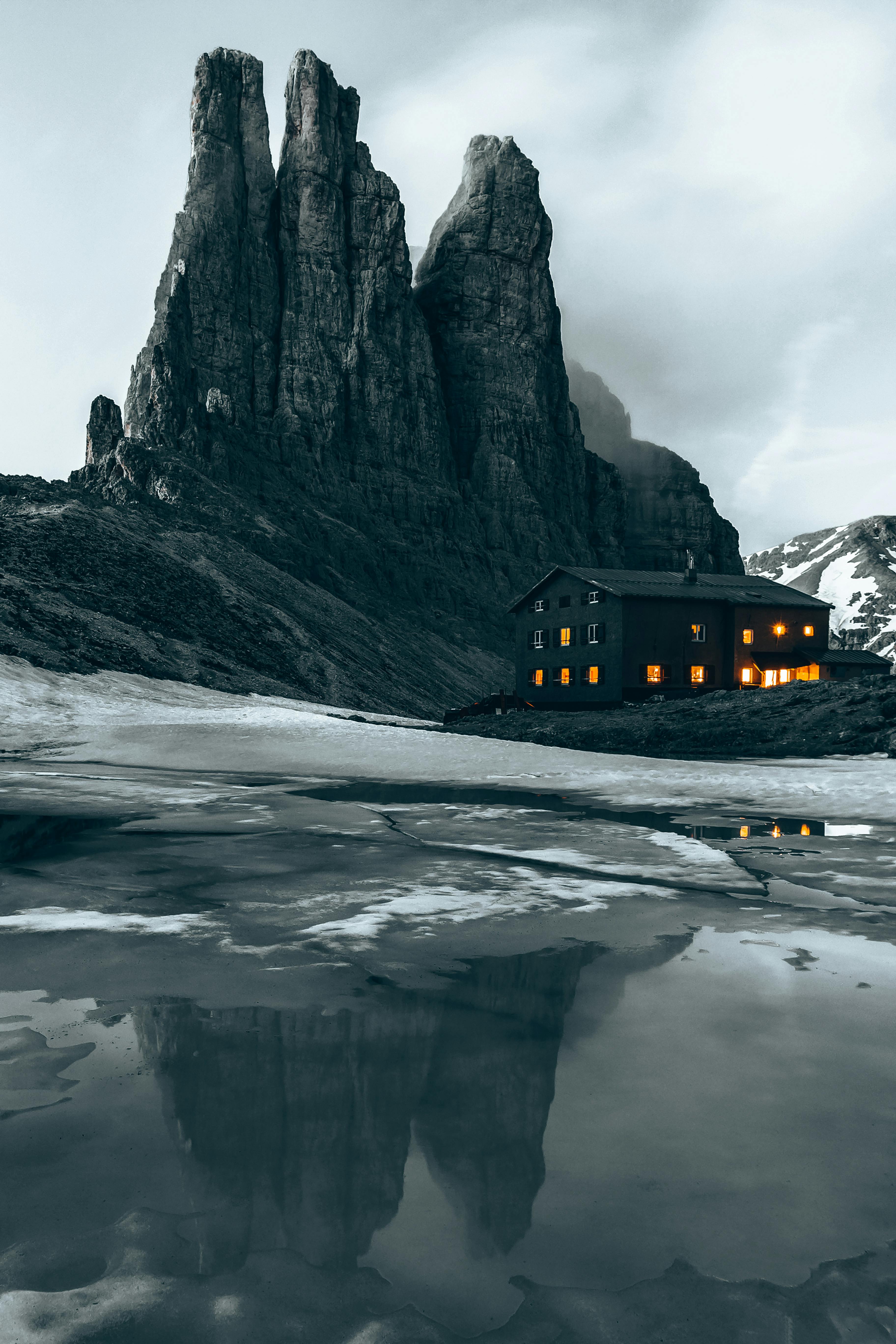 Stunning view of Vajolet Towers in the Dolomites, Italy, reflecting on icy ground with a mountain hut.
