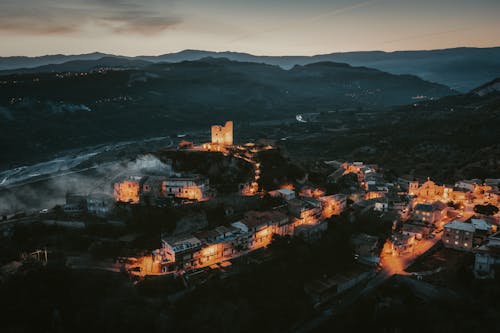 Aerial View of an Illuminated Town in Mountains with a Castle on a Hill 