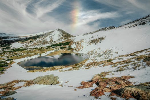 Breathtaking view of a snow-capped mountain landscape with a calm lake and vibrant sky.