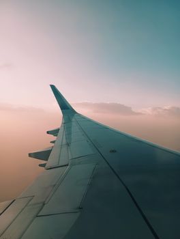 A serene view of an airplane wing flying over the soft pink and blue skies.