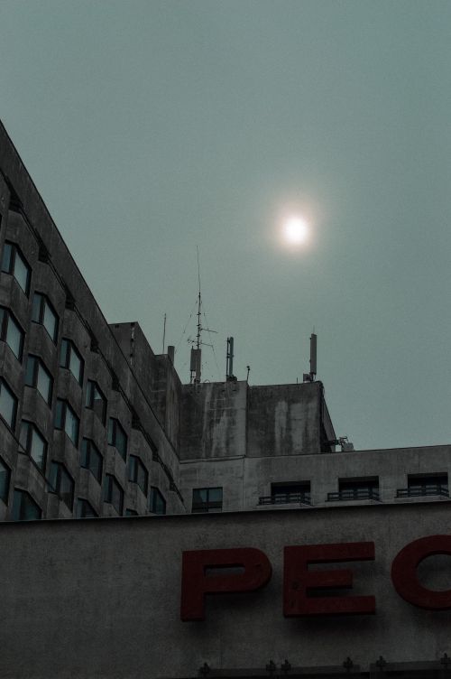 Free A striking view of brutalist buildings with the sun peeking through an overcast sky. Stock Photo