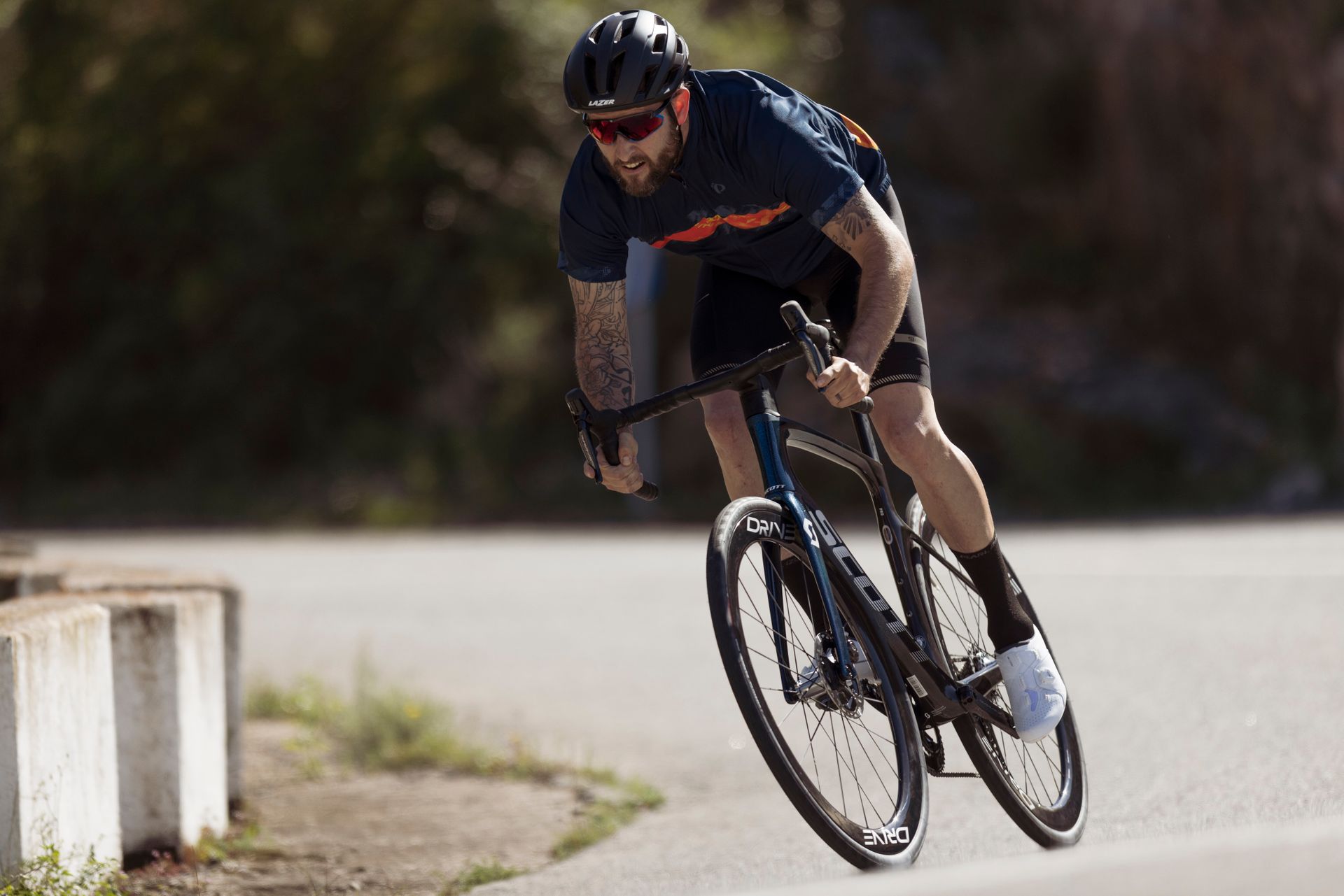 Energetic male cyclist with tattoos on a road bike, racing outdoors at high speed.