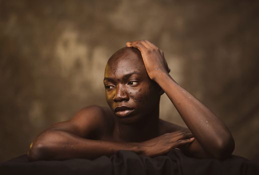 Expressive portrait of an adult man posing thoughtfully in a studio setting with a brown background.