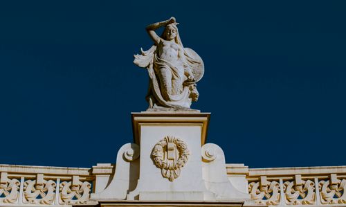 Free Intricate female sculpture atop a historic Warsaw palace, depicted under a clear blue sky. Stock Photo