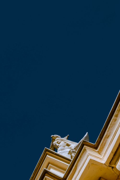 Free Statue on building corner with contrasting deep blue sky in Warsaw, Poland. Stock Photo
