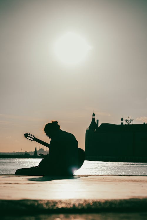 Silhouette of Person Playing Guitar Sitting Near the OCean