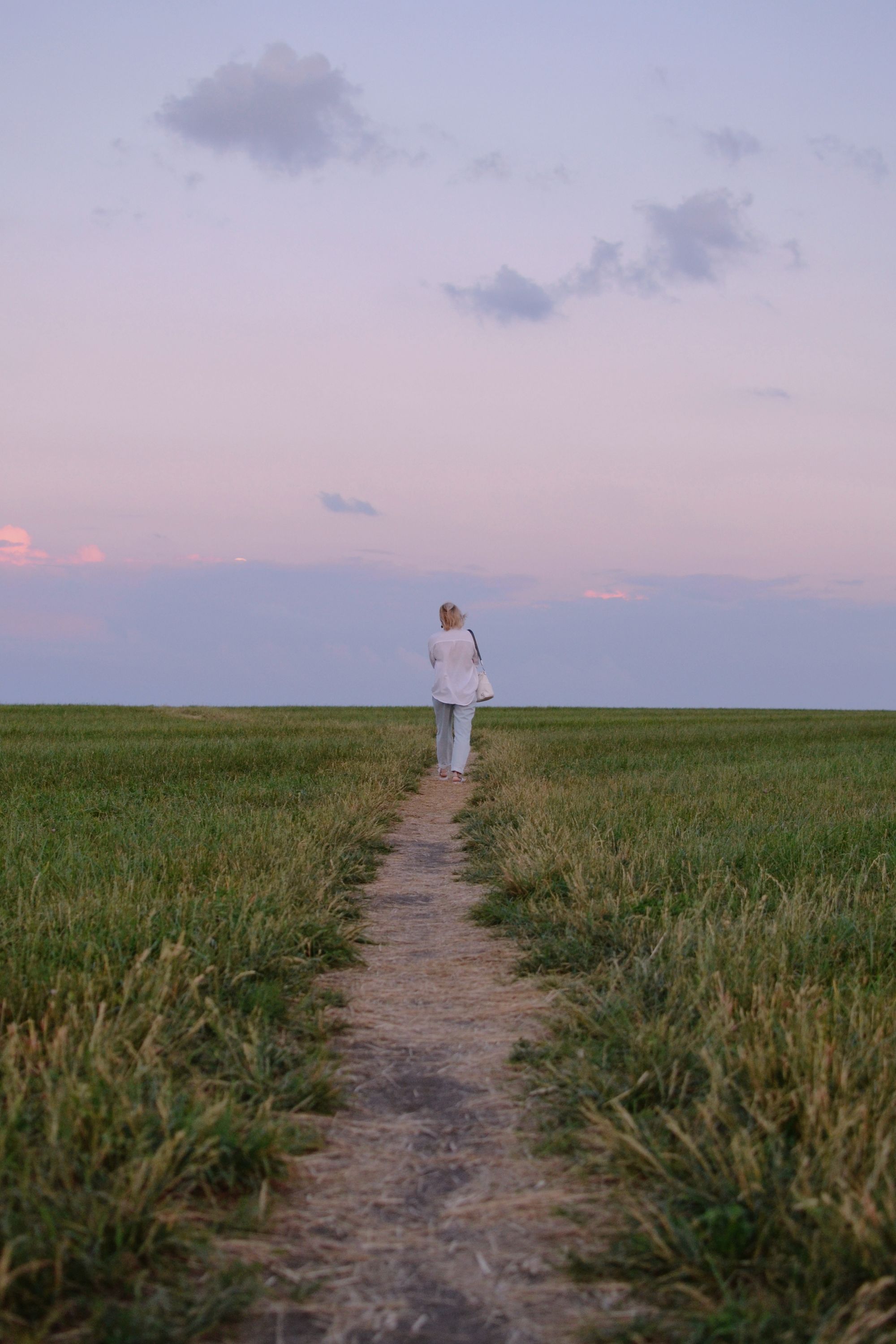 Mujer de espaldas caminando por un sendero abierto al atardecer, contraluz suave