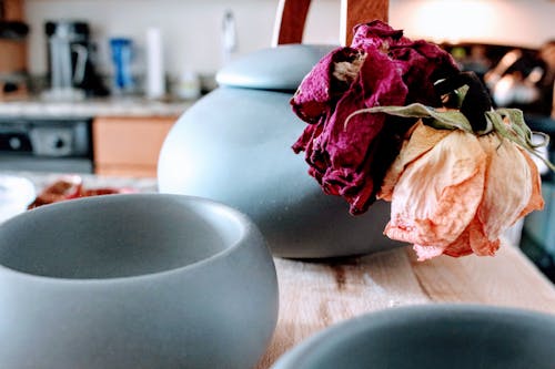 在粉红色和紫色的花瓣花附近的棕色木制的桌子上的三个圆形蓝绿色陶瓷罐