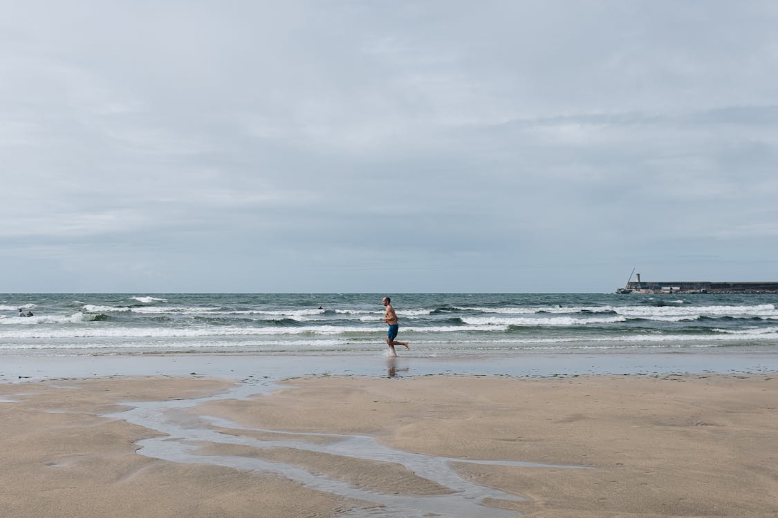 A Shirtless Man Running on the Beach