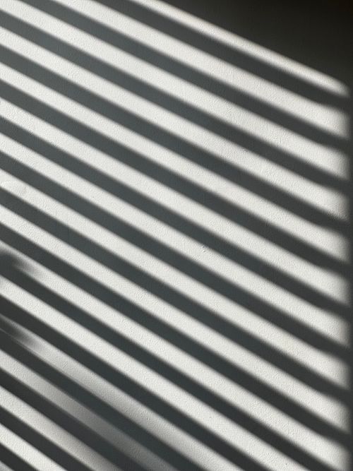 Free Play of light creating striped shadow pattern on a wall through blinds in a minimalist setting. Stock Photo