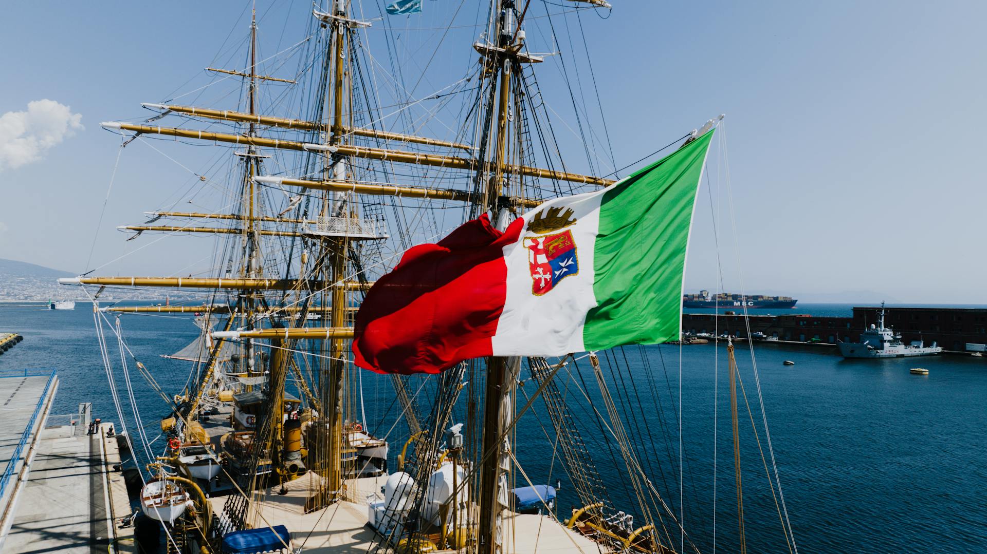 Italian naval ship with fluttering flag docked at Naples harbor, capturing nautical essence.