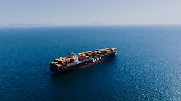 An aerial shot of a loaded container ship sailing near Naples, Italy under clear blue skies.