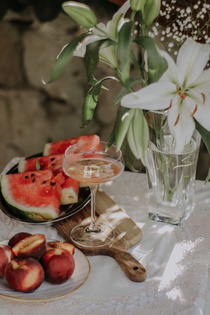 A summer cocktail on a table with watermelon slices and peaches, accented with a lily bouquet.