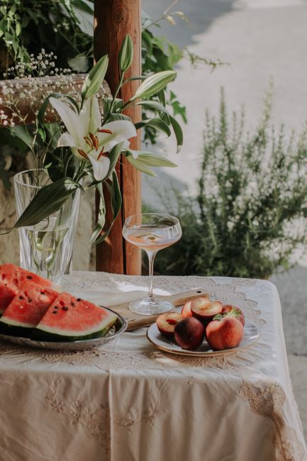 A tranquil summer scene with watermelon, peaches, and lilies on lace-covered table.