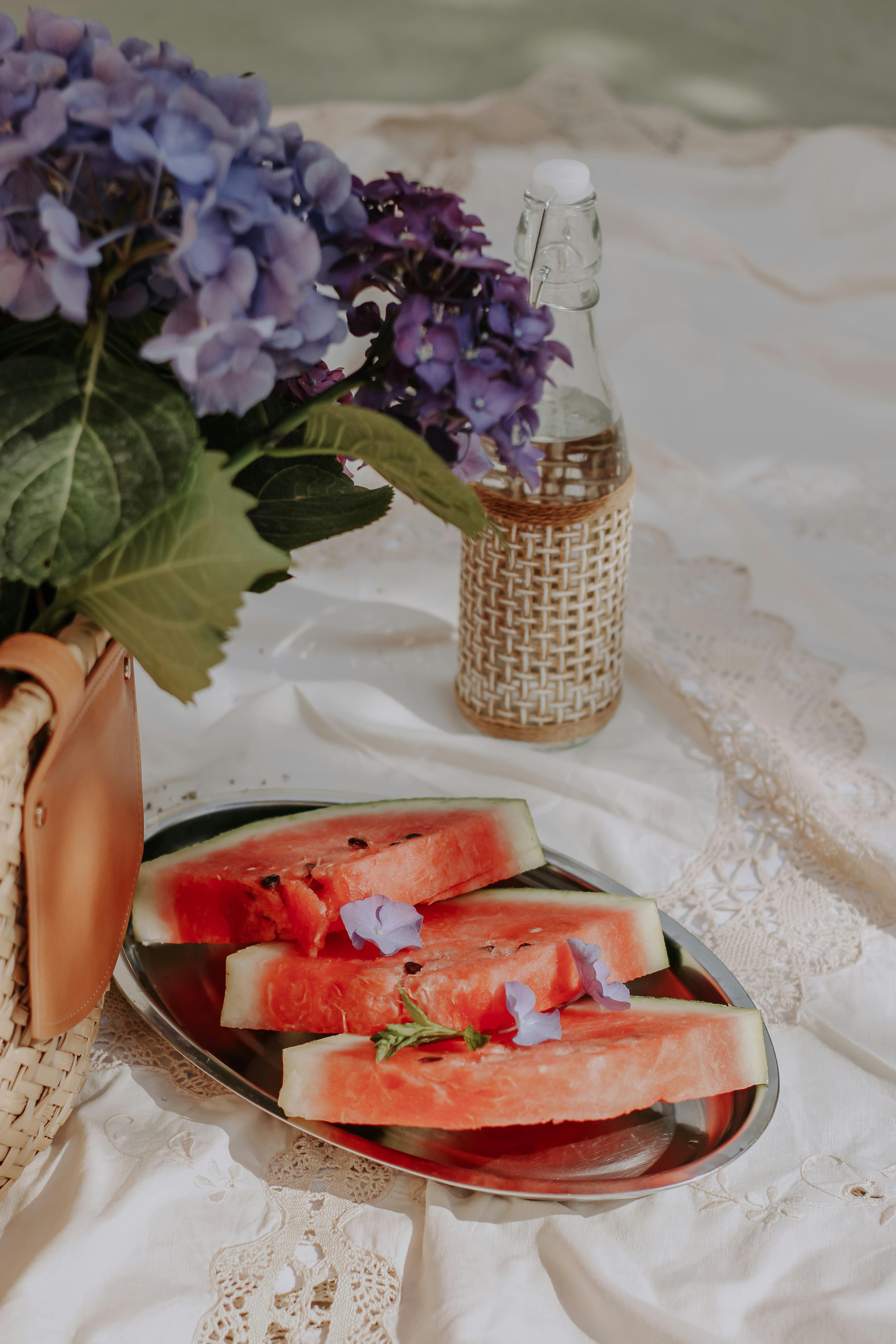 Free Fresh watermelon slices with hydrangeas on a lace tablecloth, evoking a summer picnic vibe. Stock Photo