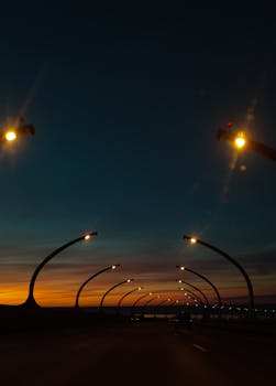 A scenic view of a bridge with curved streetlights illuminated under a twilight sky.