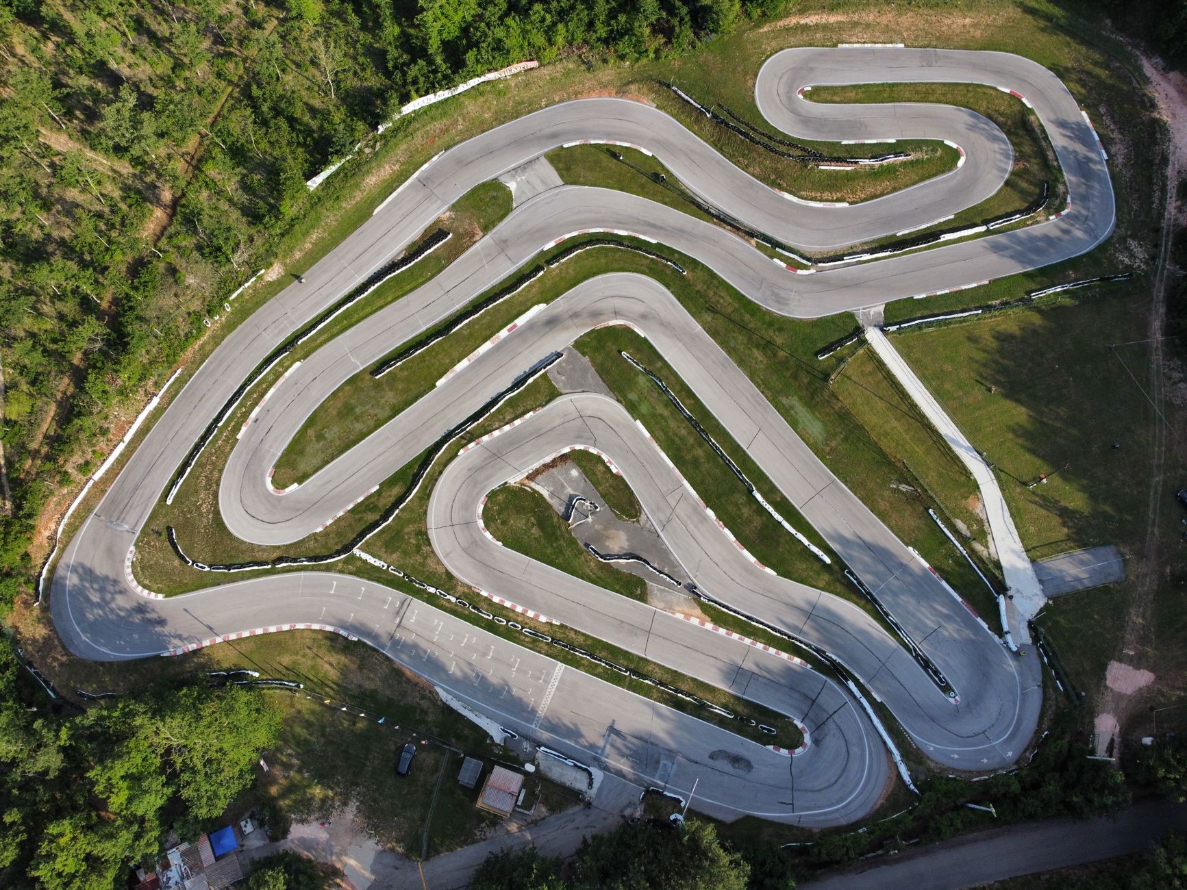 Drone shot of a winding racetrack surrounded by lush greenery from a bird's eye perspective.