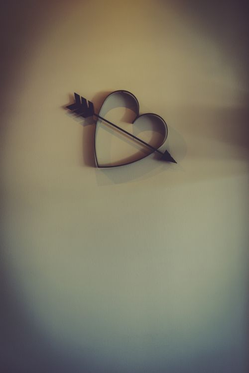 Free Artistic heart shape pierced by an arrow on a minimalist wall, offering a modern design aesthetic. Stock Photo