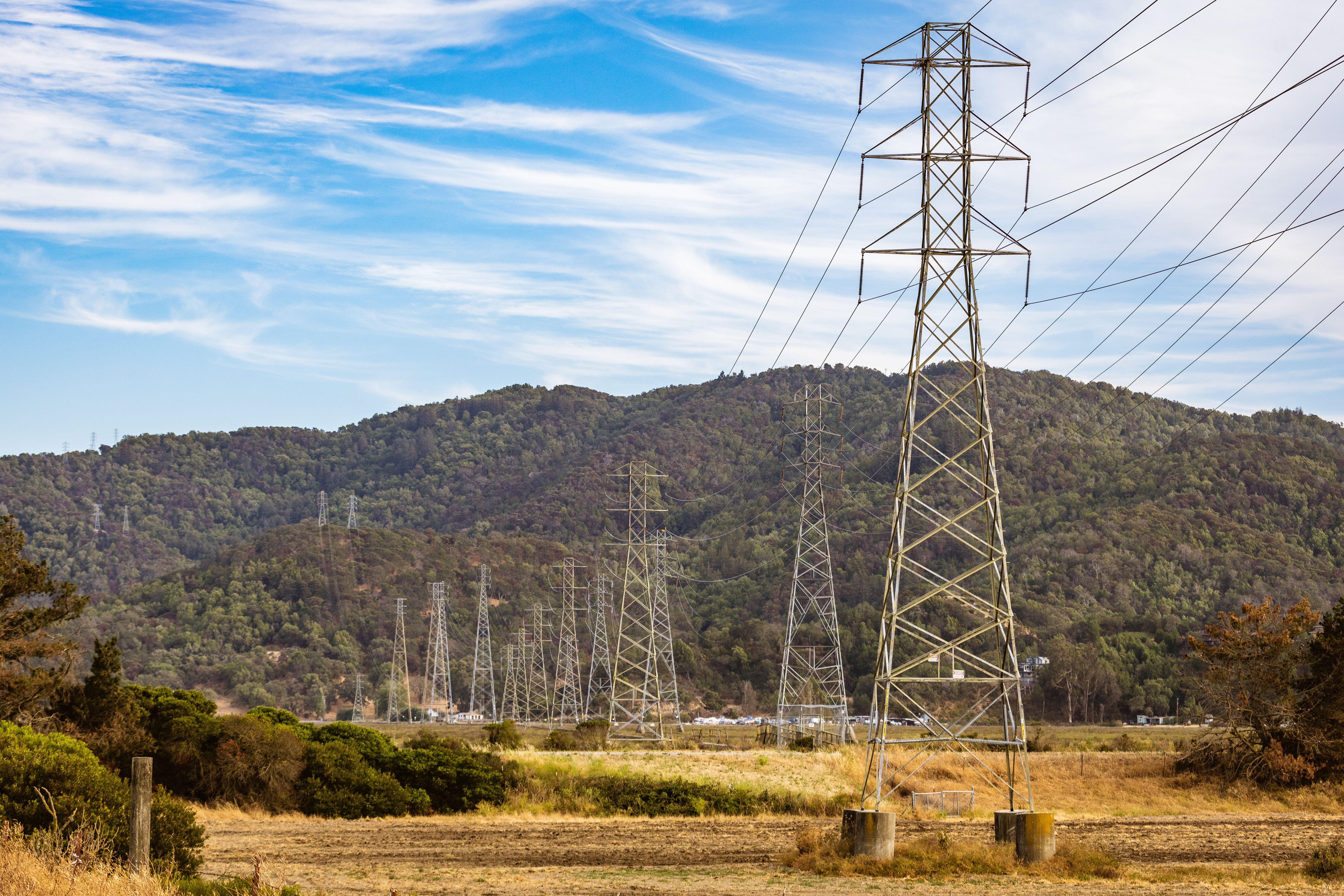 Scenic view of power lines crossing a field with green mountains and a blue sky.