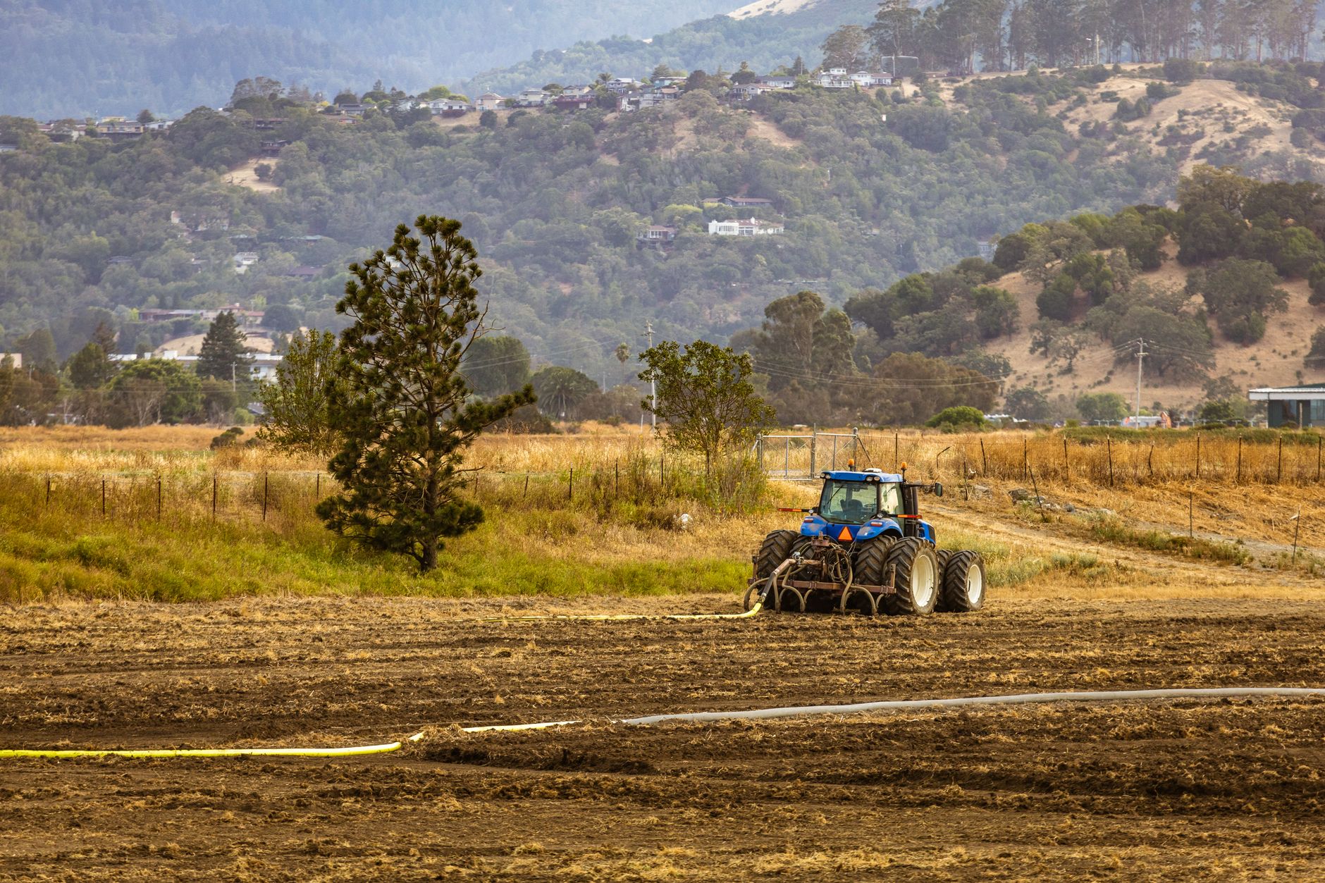 Blue tractor working on plowing a field in a scenic rural landscape during the day.
