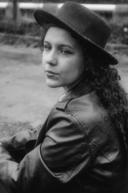 Grayscale Photo of a Woman in a Black Leather Jacket and Hat