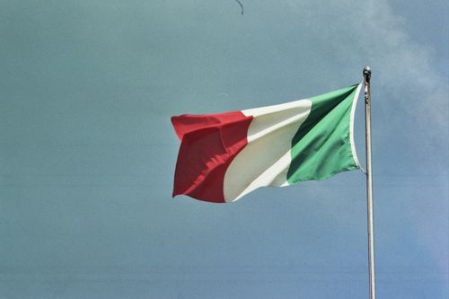 Free Italian flag flying proudly on a flagpole set against a bright blue sky. Symbol of Italy. Stock Photo