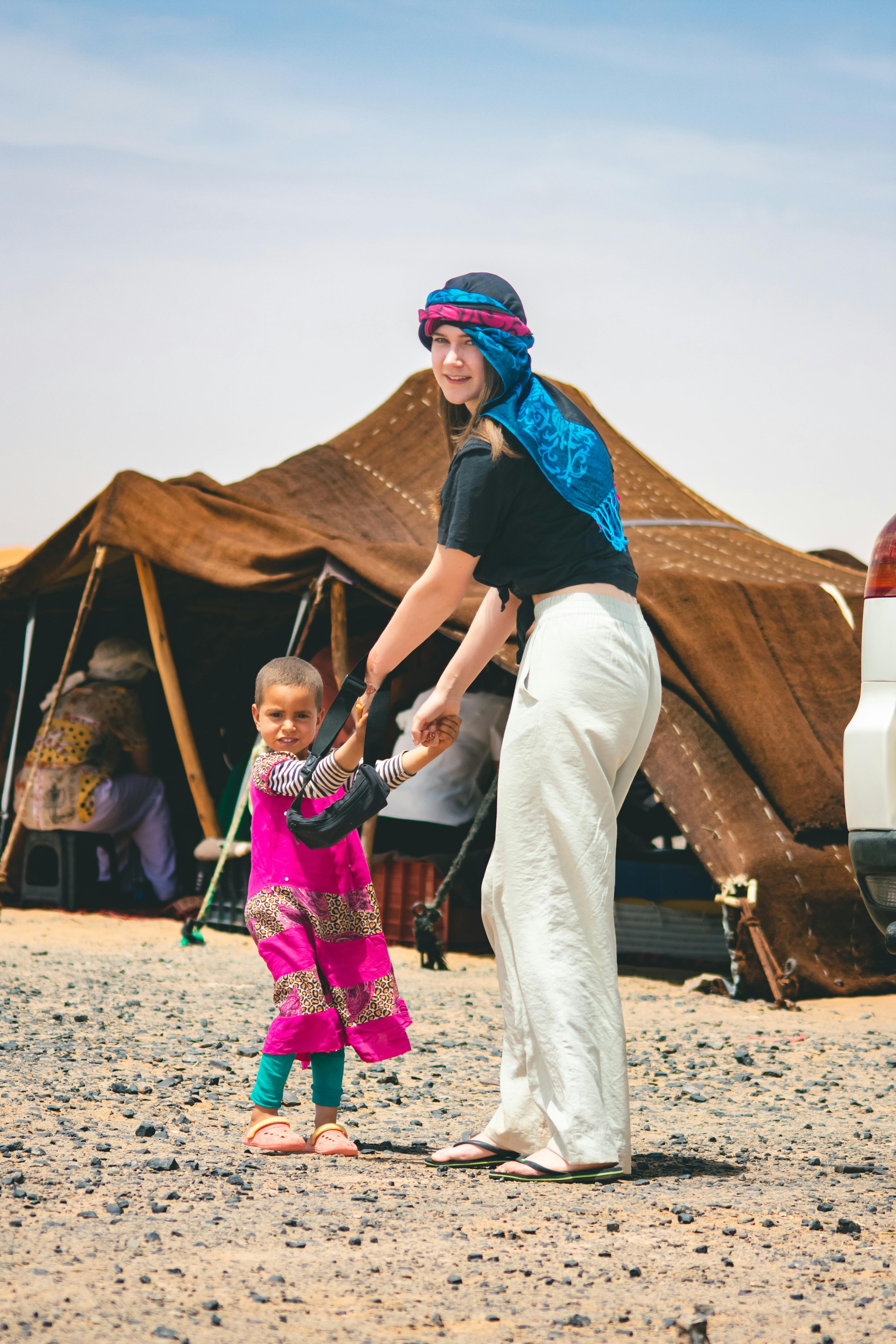 Smiling woman and child holding hands in a Moroccan desert camp.