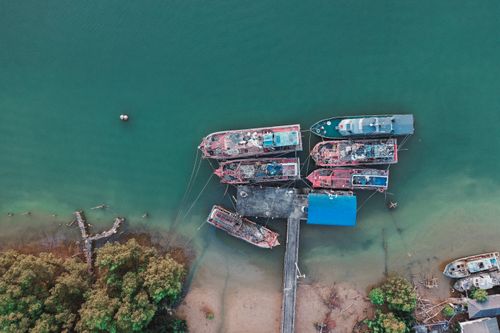 Free Aerial shot of boats docked along a picturesque coastline with lush greenery and clear waters. Stock Photo