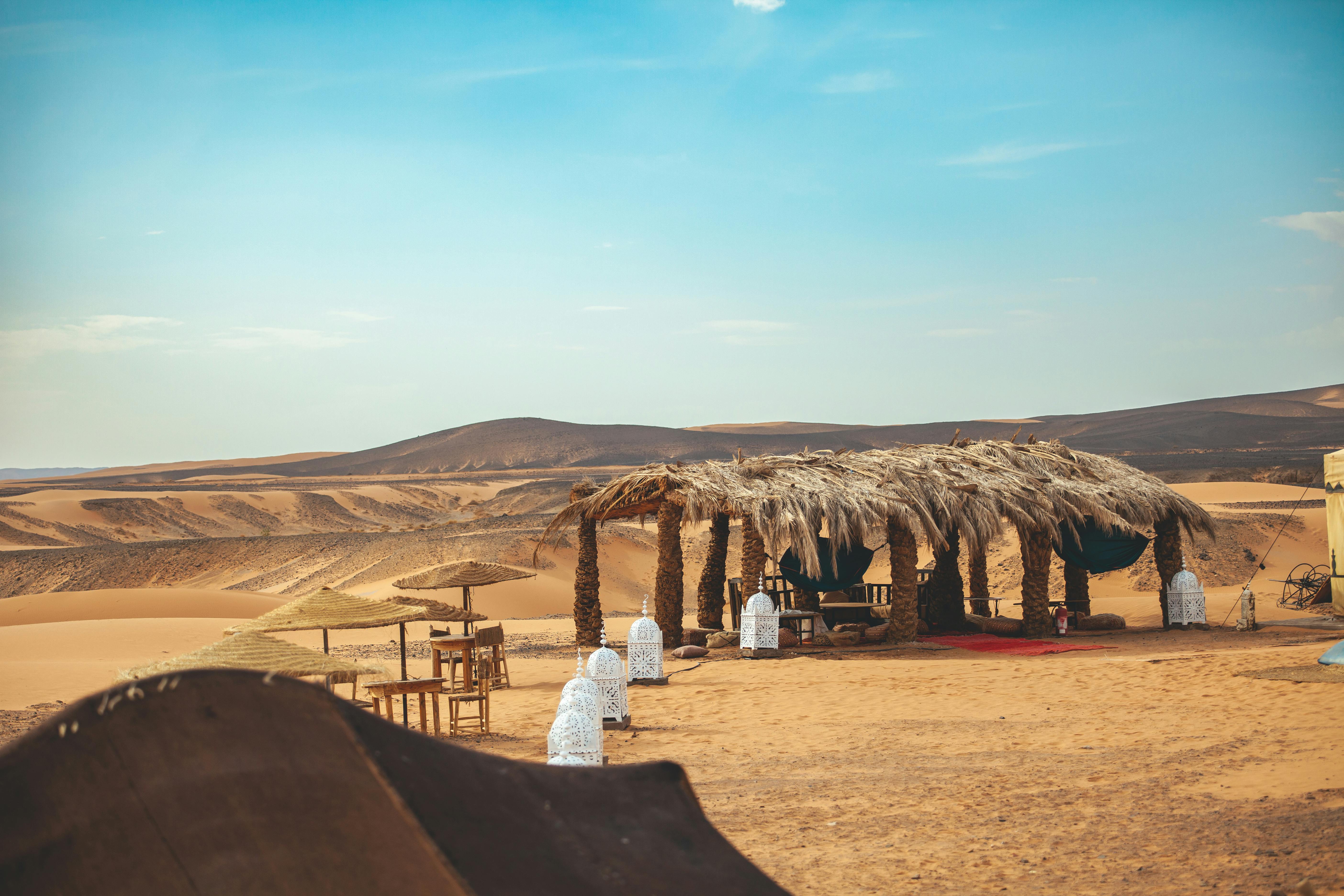 Captured in Morocco's Merzouga, this desert oasis features a traditional rustic shelter amidst sand dunes.