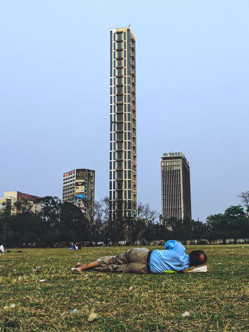 Free A man lying on grass, resting in an urban park with city skyscrapers in the background. Stock Photo