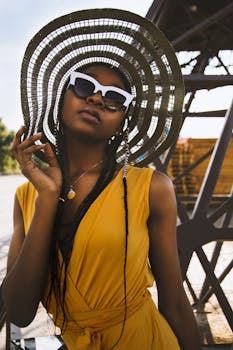 Fashionable black woman posing outdoors in a yellow dress and sunglasses.